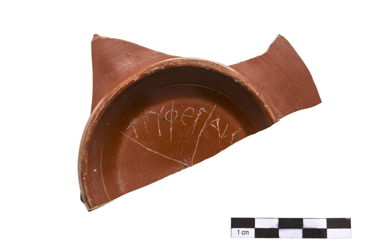Fragment eines roten Keramiktellers mit eingeritzter Inschrift in griechiscgen Buchstaben.