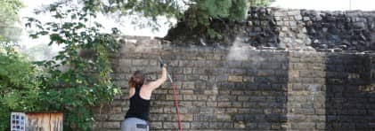 Eine Frau reinigt mit einem Gerät die römische Mauer. Rechts ist ein heller Streifen zu sehen.