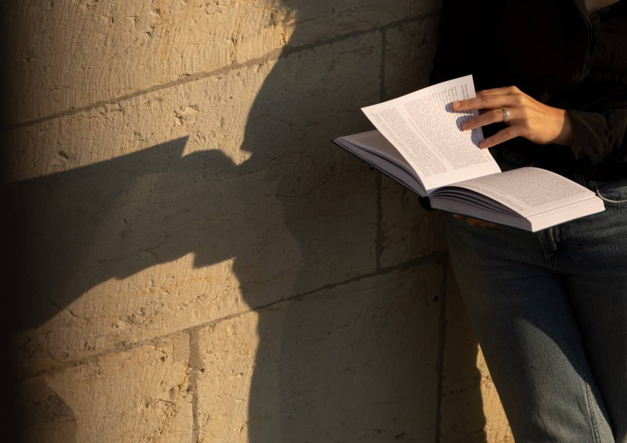 Foto einer Person vor einer sonnigen Wand, die ein Buch hält.