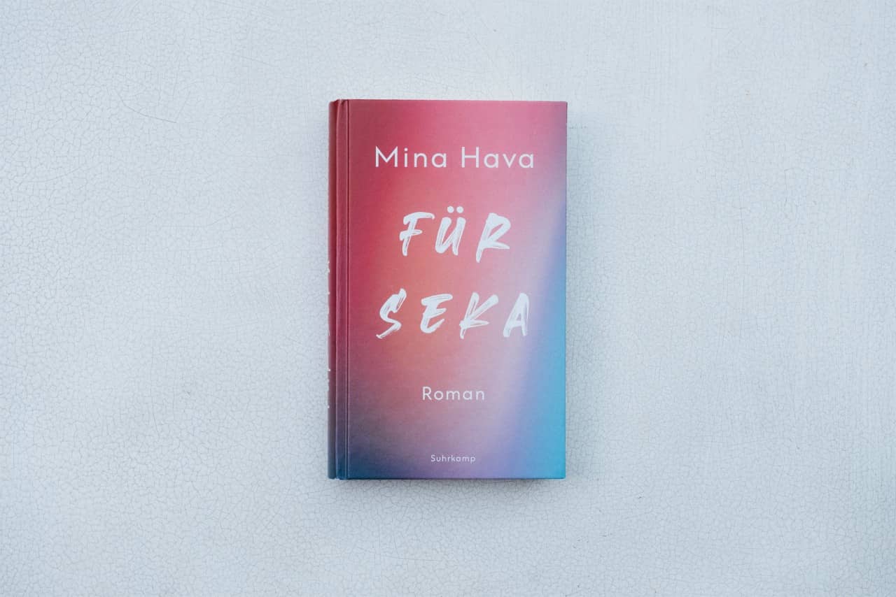 Das Buchcover mit dem mit einem dicken Marker handgeschriebenen Titel "Für Seka" besteht aus einem Farbverlauf in den Farbtönen pink, orange bis blau. Das Buch liegt auf einem weiss lackierten, krakelierten Untergrund.