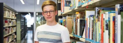 Junge mit Brille sthet vor Büchergestell