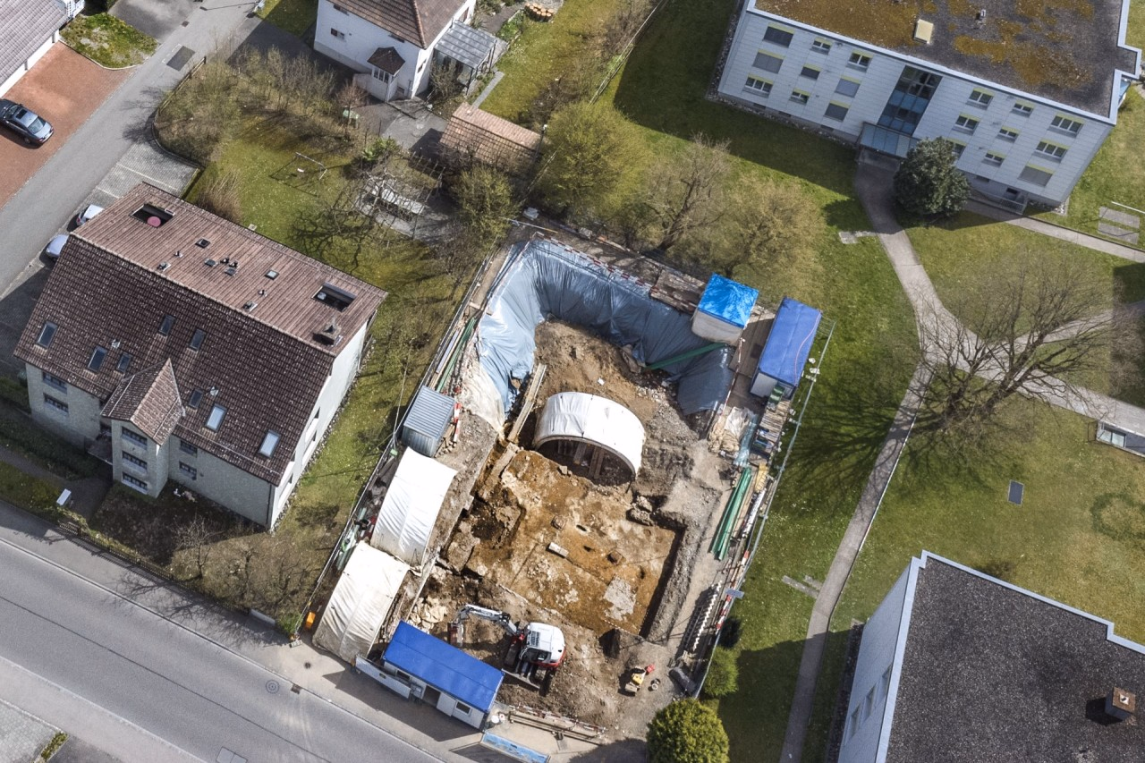 Eine Ausgrabungsfläche mit weissen Bogenzelten inmitten eines Wohnquartiers.