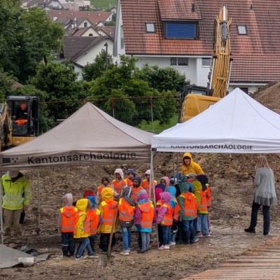 Eine Gruppe Kindergartenkinder steht unter einem Grabungszelt.