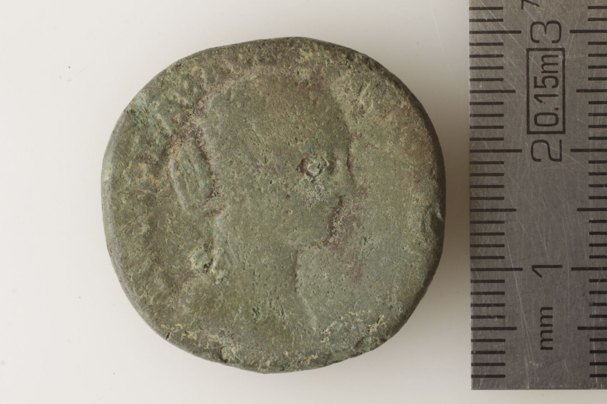 Grün angelaufene Münze mit kaum mehr sichtbarem Münzbild, das jedoch eine Frau mit Haarknoten erahnen lässt.
