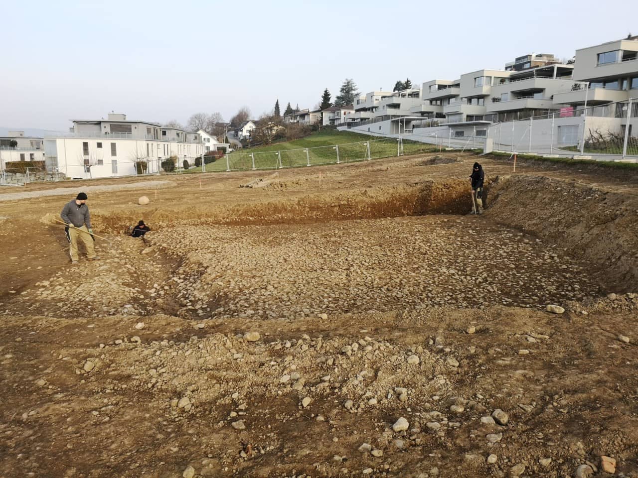 Blick auf die ausgegrabene römische Strasse mit drei Mann Grabungsteam.