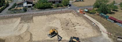 Blick auf die Grabungsfläche. Der Hausgrundriss ist mit Holzpfosten markiert.