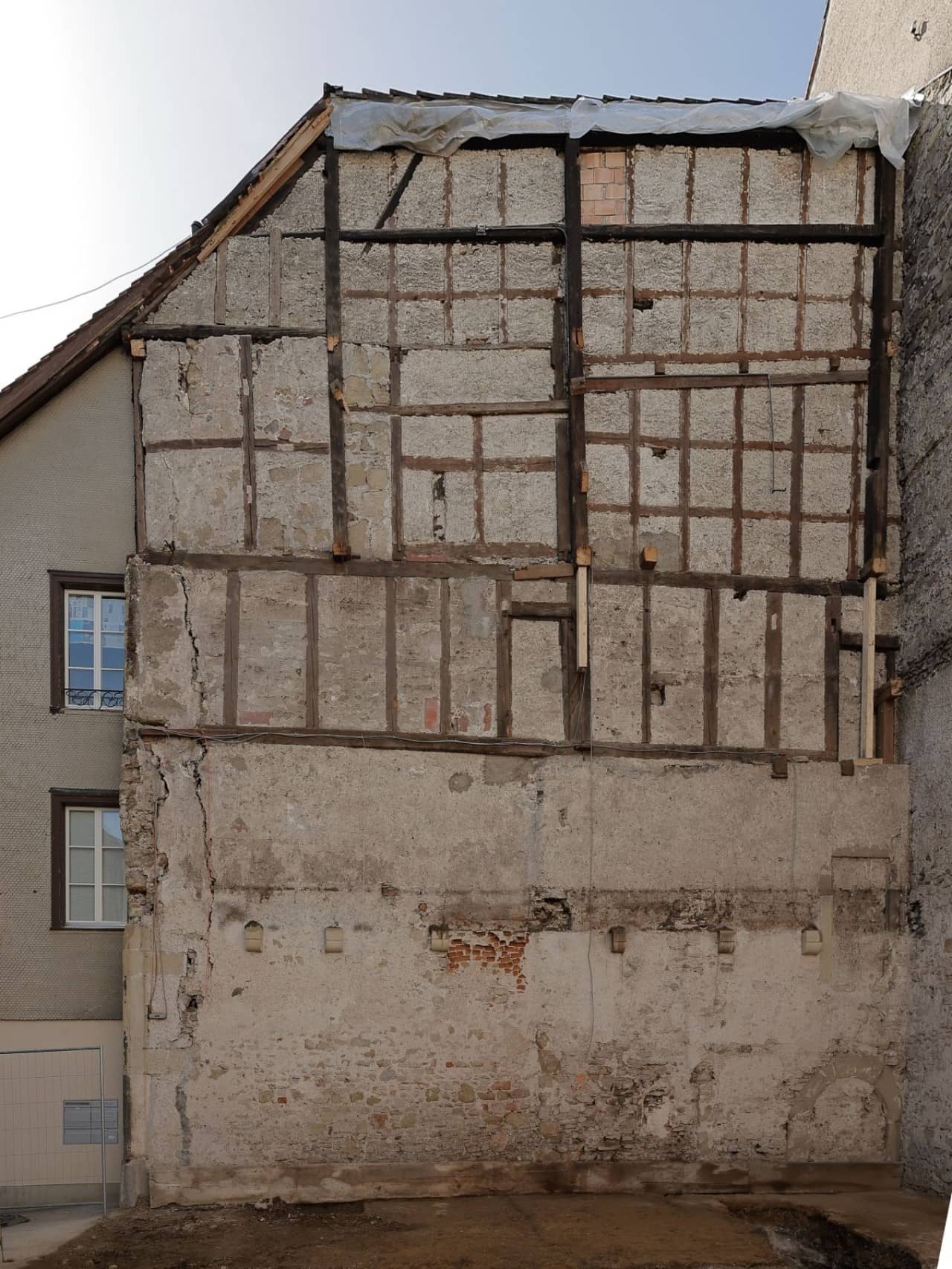 Blick auf die Innenseite einer Hauswand mit Balken und weissem Vertputz dazwischen.