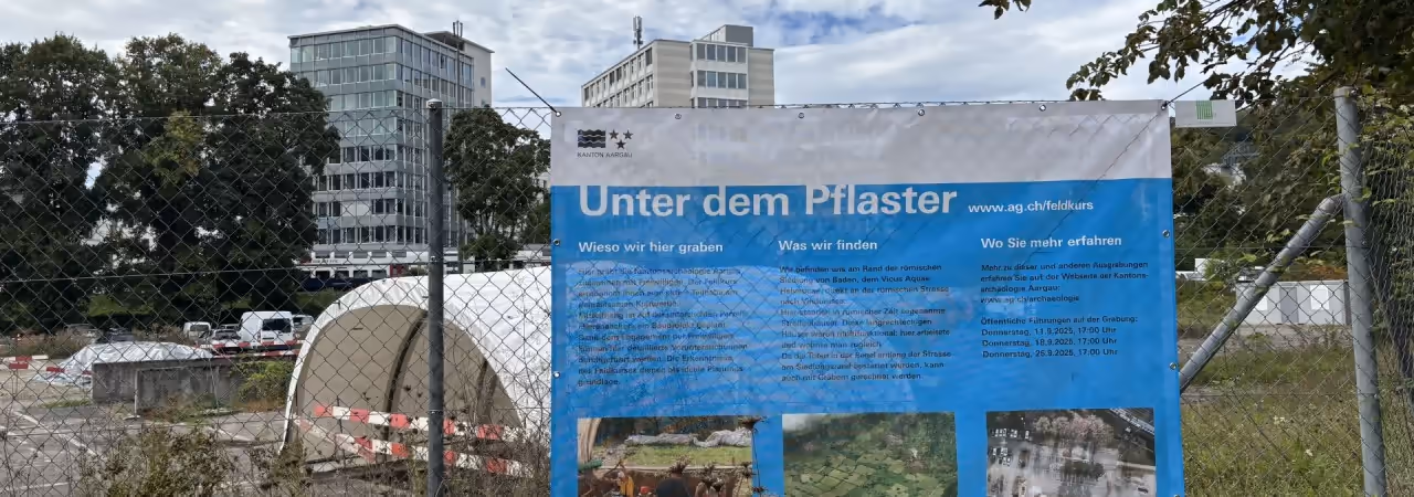 Blick auf das Ausgrabungszelt auf dem Parkplatz, im Vordergrund die Infoplache der Kantonsarchäologie.
