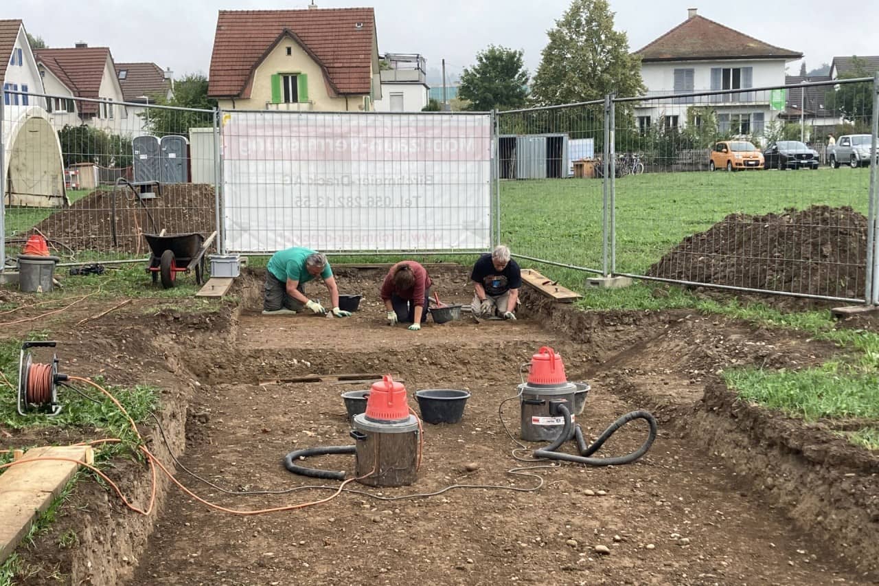 Drei Freiwillige legen präparieren eine Fläche auf dem archäologischen Feldkurs. Im Vordergrund zwei Staubsauger.