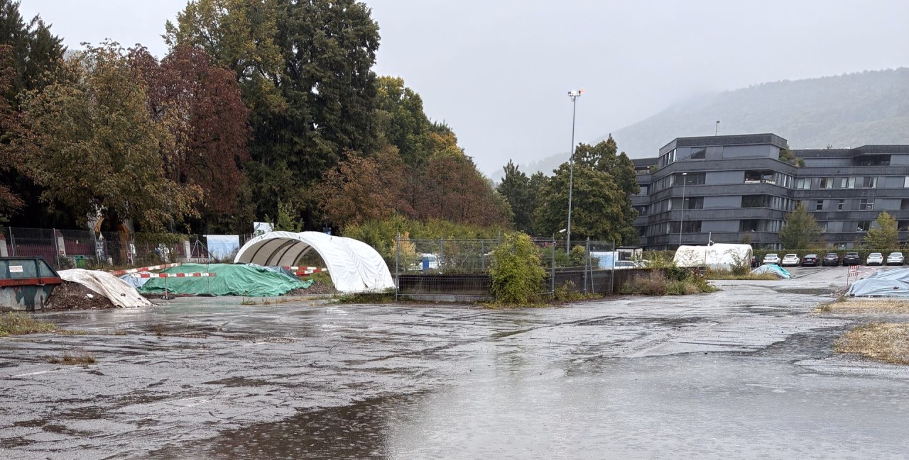 Parkplatz mit weissen Bogenzelten, die in strömendem Regen stehen.