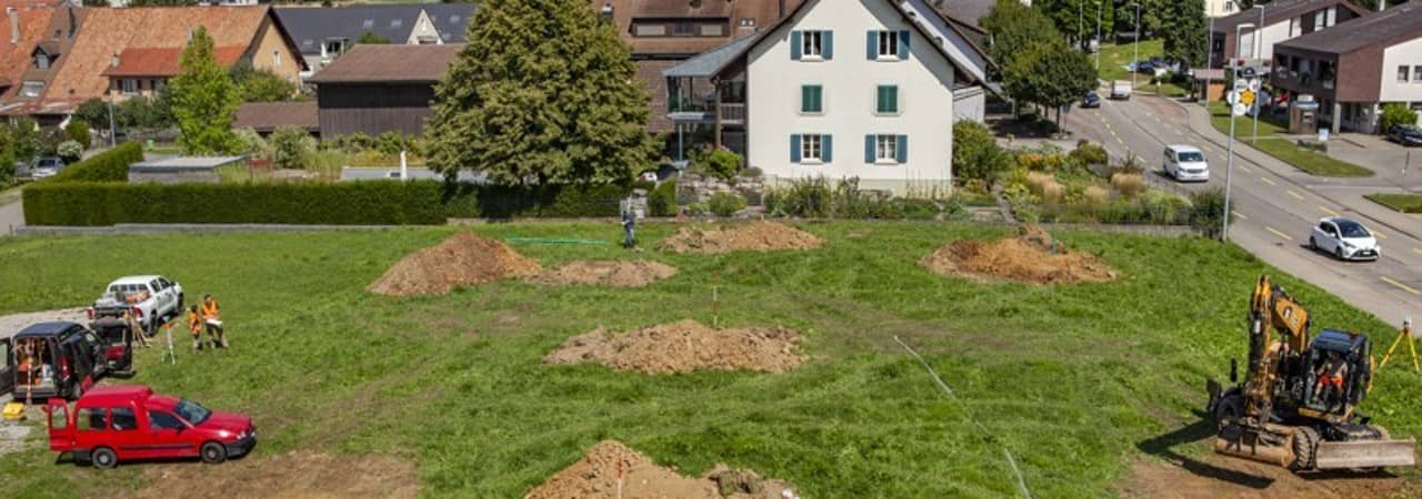 Blick auf die Grabungsfläche auf einer grünen Wiese.