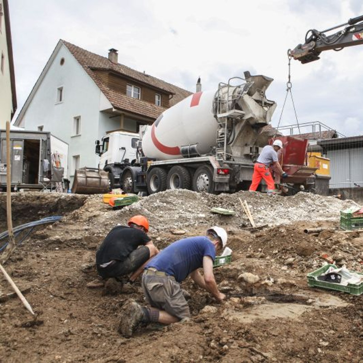Zwei Ausgräber an der Arbeit, rechts im Bild ein Bagger.