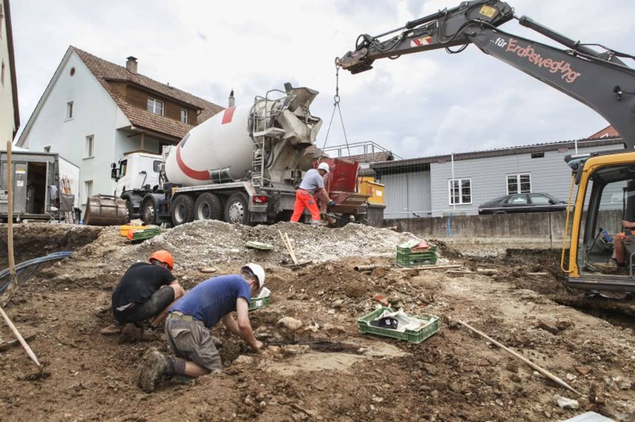 Zwei Ausgräber an der Arbeit, rechts im Bild ein Bagger.