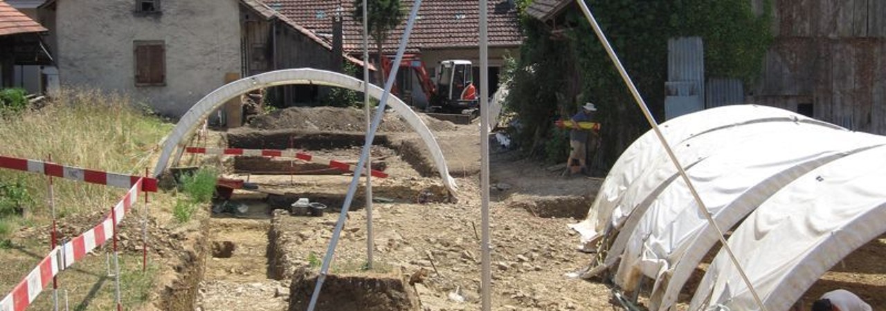 Rechts im Bild weisse Grabungszelte und links die Grabungsfläche.