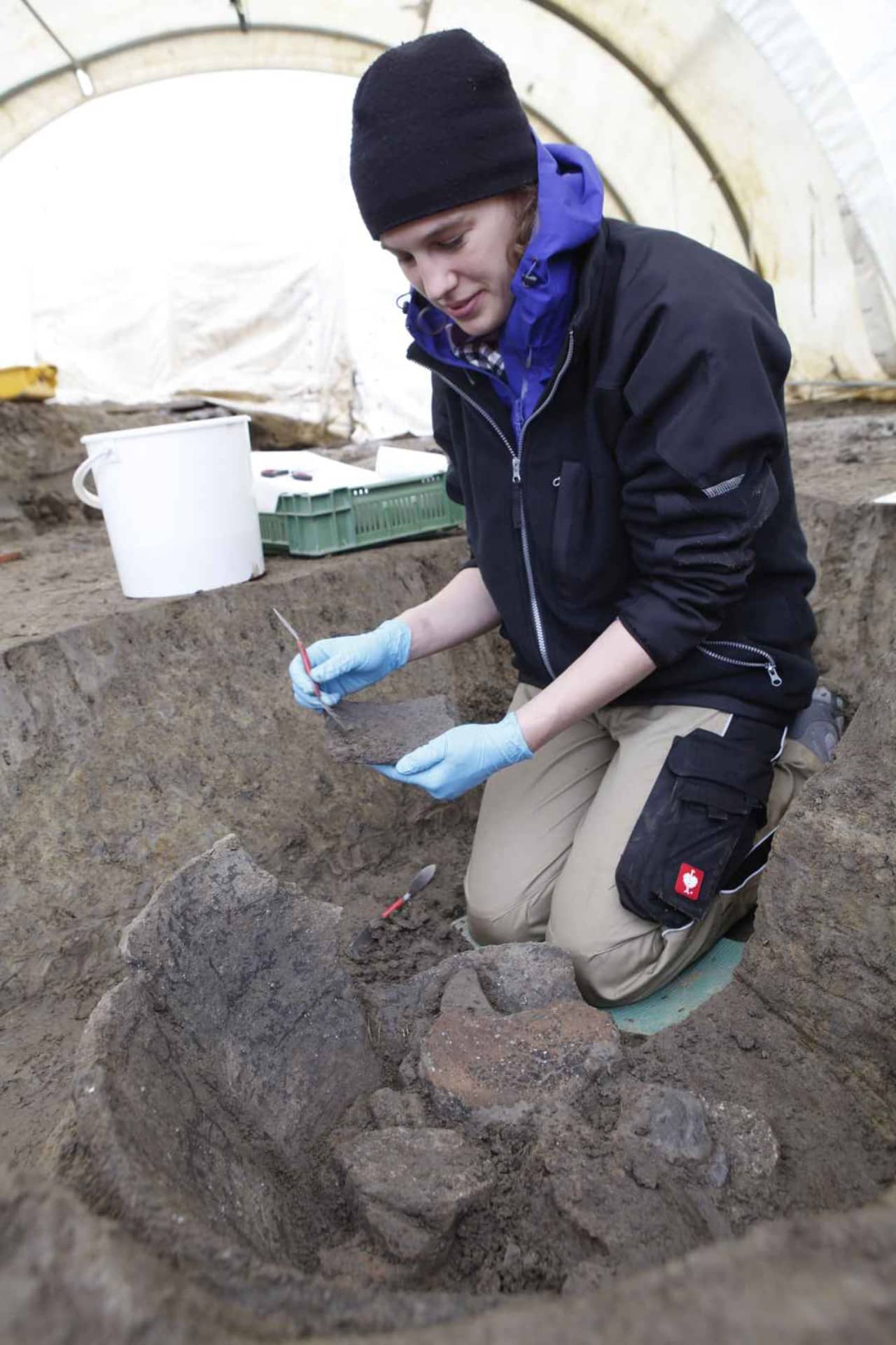 Eine Restauratorin gräbt einen in den Boden eingegrabenen Vorratstopf aus der Mittelbronzezeit aus. 