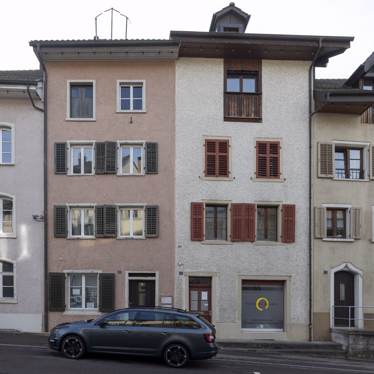 Zwei schmale Altstadthäuser mit je vier STockwerken, links altrosa Fassade, rechts weisse Fassade.