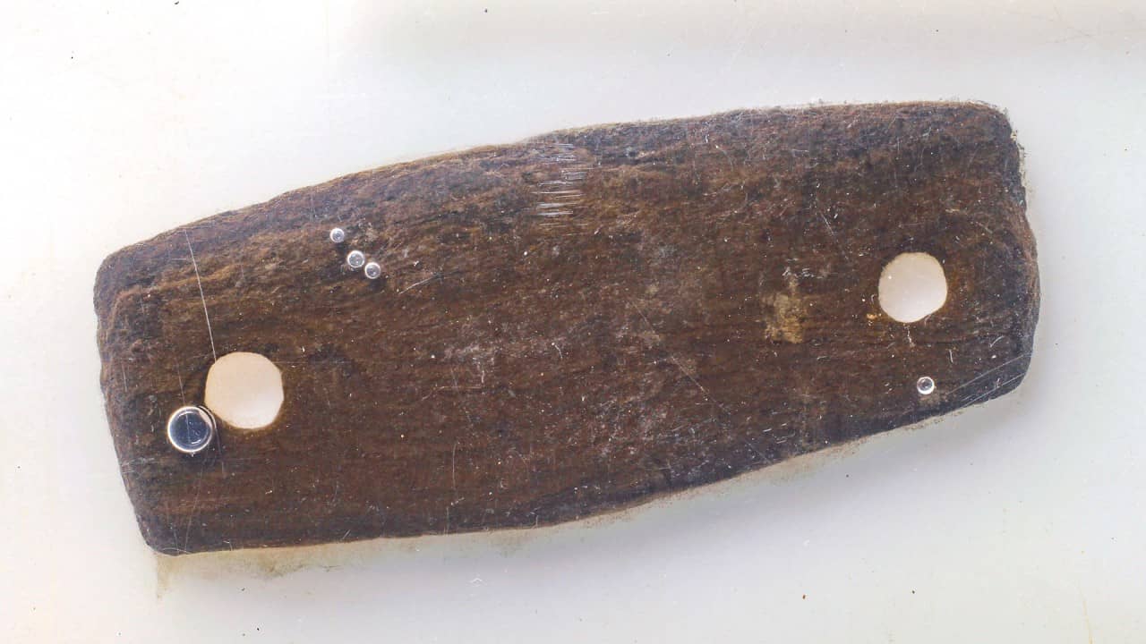 Ein langrechteckiges Holzstück mit je einem Loch am Schmalende.