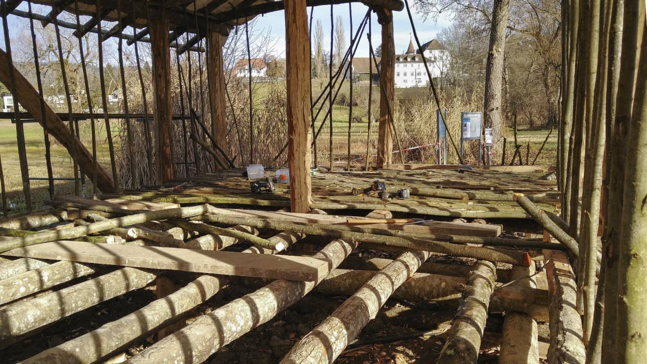 Blick ins Innere des Pfahlbauhauses mit noch nicht verputzten Wänden und einem Bohlenboden.