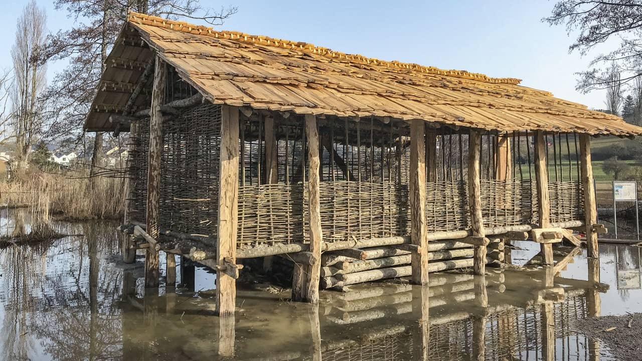 Das fertige, aber noch nicht verputzte Pfahlbauhaus in knöcheltiefem Wasser.