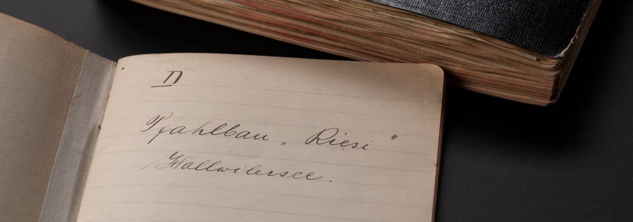 Ein aufgeschlagenes Tagebuch mit dem Schriftzug "Pfahlbau RIesi Hallwilersee" in Schnörkelschrift.
