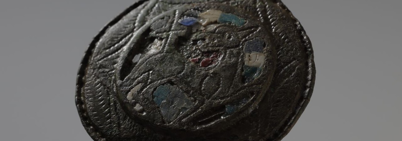 Eine Scheibenfibel mit farbigen Glaseinlagen und der Darstellung eines Lamms. 