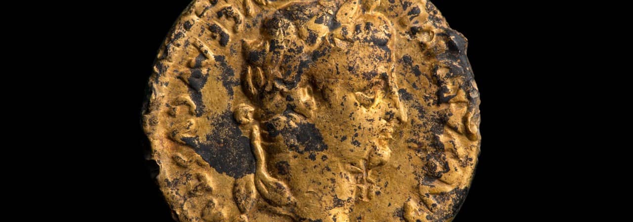 Goldene Münze mit Kaiserporträt vor schwarzem Hintergrund.
