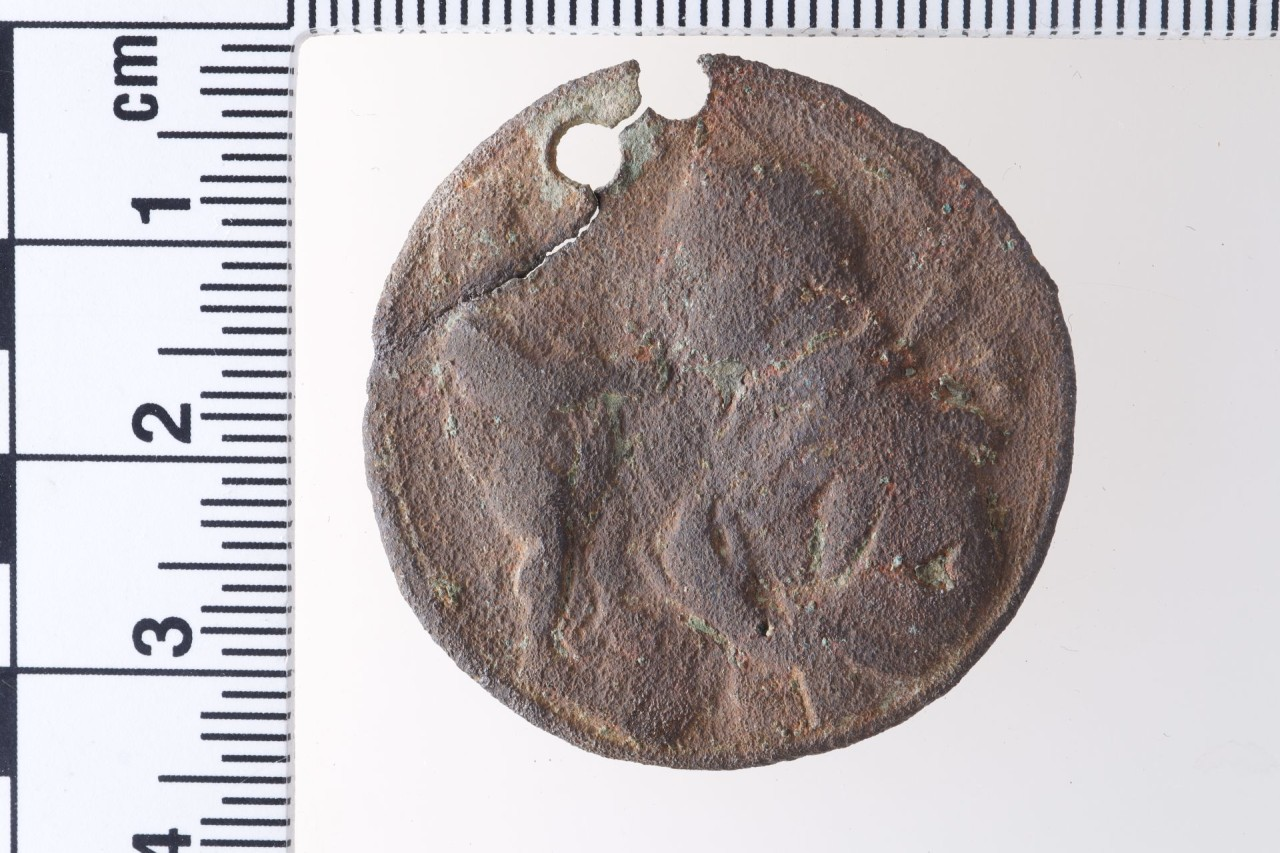 Rundes, braun korrodiertes Heiligenabzeichen mit der unscheinbaren Darstellung einer Figur, die ein Kind auf den Armen trägt.