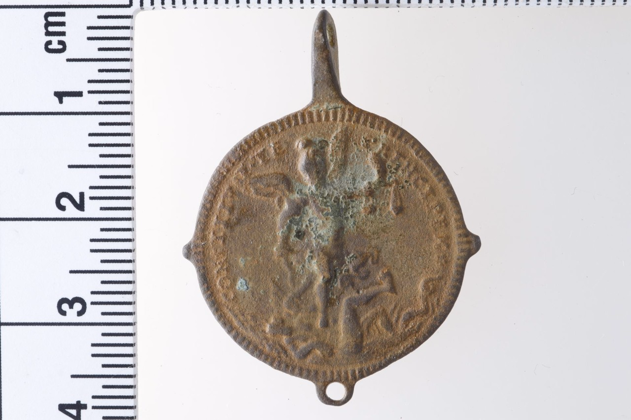 Rundes, braun korrodiertes Pilgerzeichen mit der Darstellung einer geflügelten FIgur.
