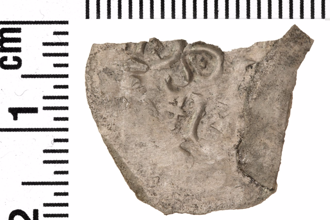 Fetzenartig sehr flache Silbermünze mit eingeprägten Buchstaben. 