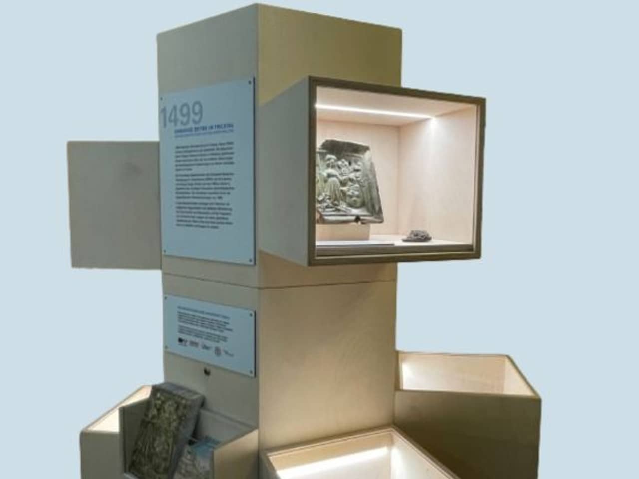 Vitrine aus hellem Holz mit kleinen hell erleichteten Sichtfenstern, in denen archäologische Funde zu sehen sind.