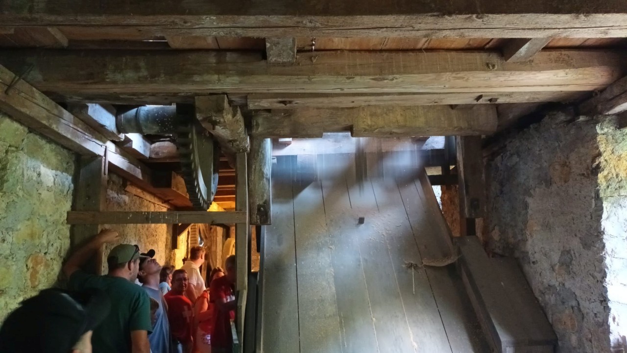Mehrere Personen stehen in der historischen Säge mit einer schrägen Holzrampe, Steinwänden und sichtbaren Balkenkonstruktionen. Licht fällt durch eine Öffnung.