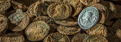 Römische Münzen in unrestauriertem Zustand, eine glänzende restaurierte Münze darauf.