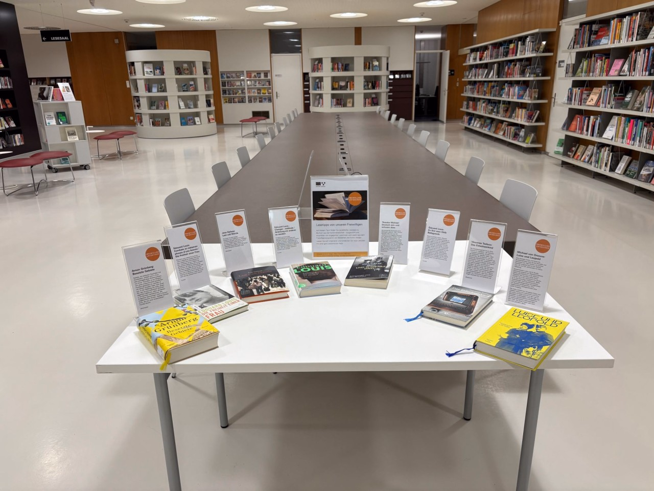 Aufsteller mit handgeschriebenem Text auf einem Tisch. Vor den Aufstellern liegt jeweils ein Buch.