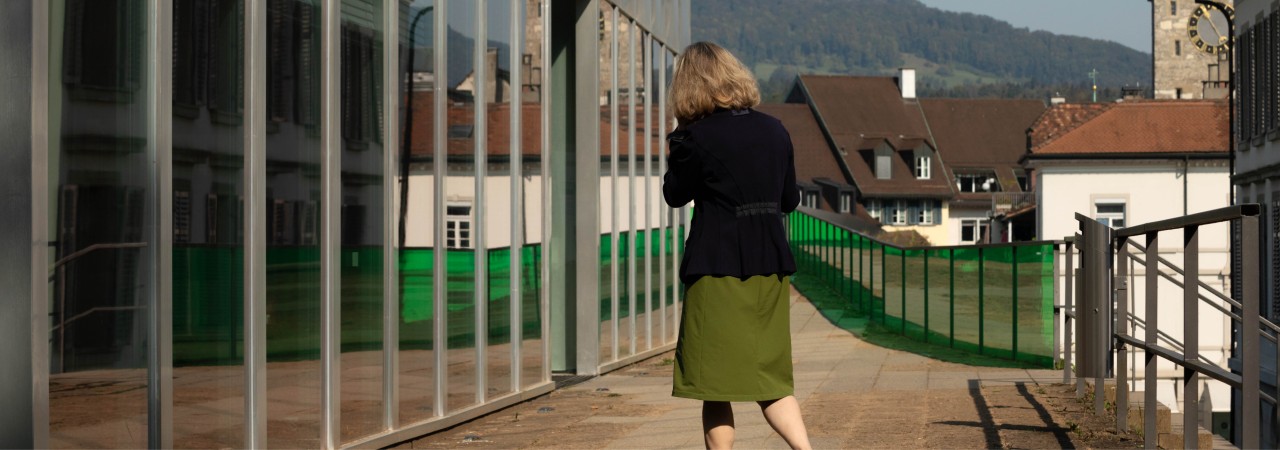 Frau mit grünem Rock vor einem Gebäude mit Glasfassade.