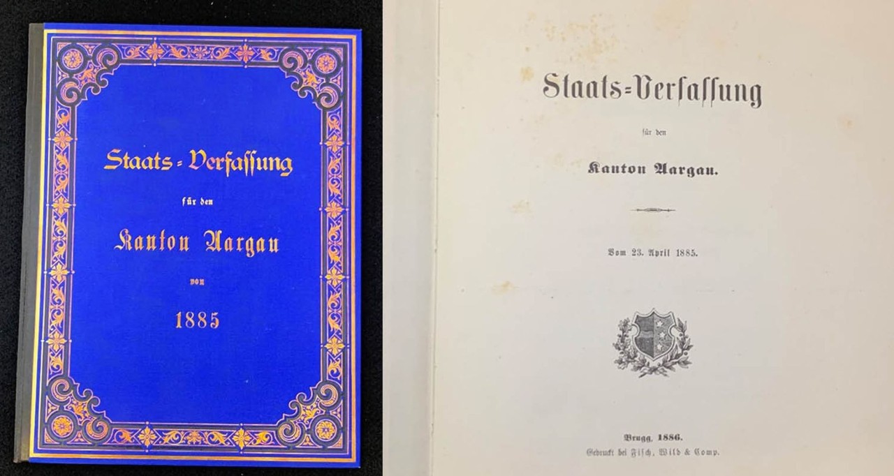 Auf der linken Seite: Staatsverfassung von 1885 mit blauem Einband und goldenem Zierrand. Auf der rechten Seite: Titelblatt Staatsverfassung von 1885 in alter Schrift mit kleinem Wappen auf der unteren Hälfte.