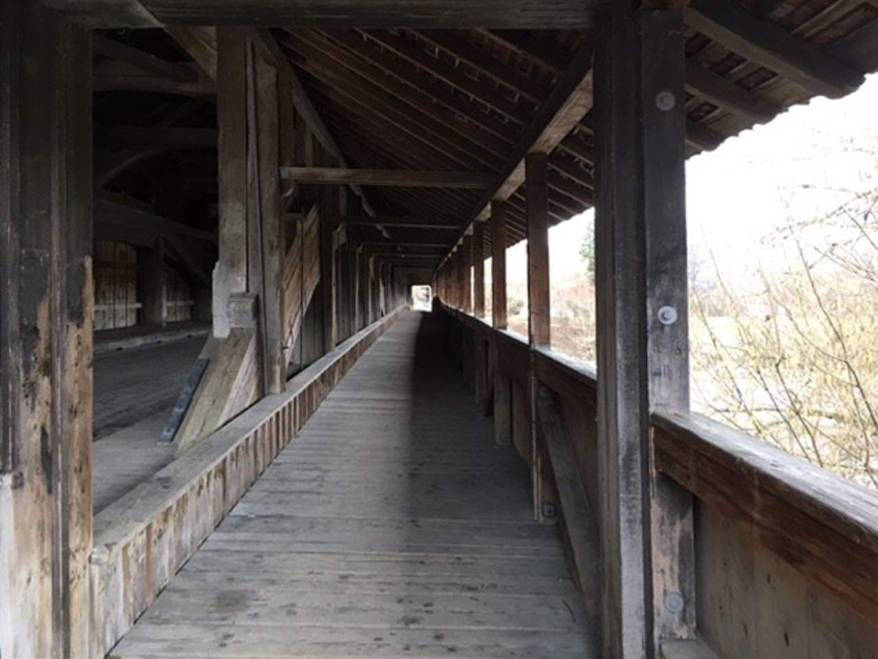 Blick durch eine Holzbrücke mit Fenstern nach draussen zum Fluss.