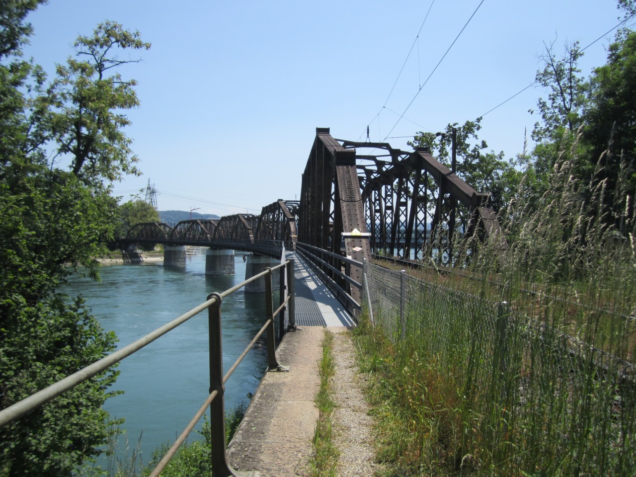 Farbfoto mit Blick über eine geschwungene Stahlbrücke über einen Fluss.