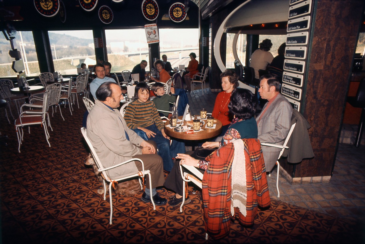 Alte Farbaufnahme mit Personen in einem Autobahn-Restaurant, das als Brücke über die Autobahn führt. mit Blick auf die Autobahn.