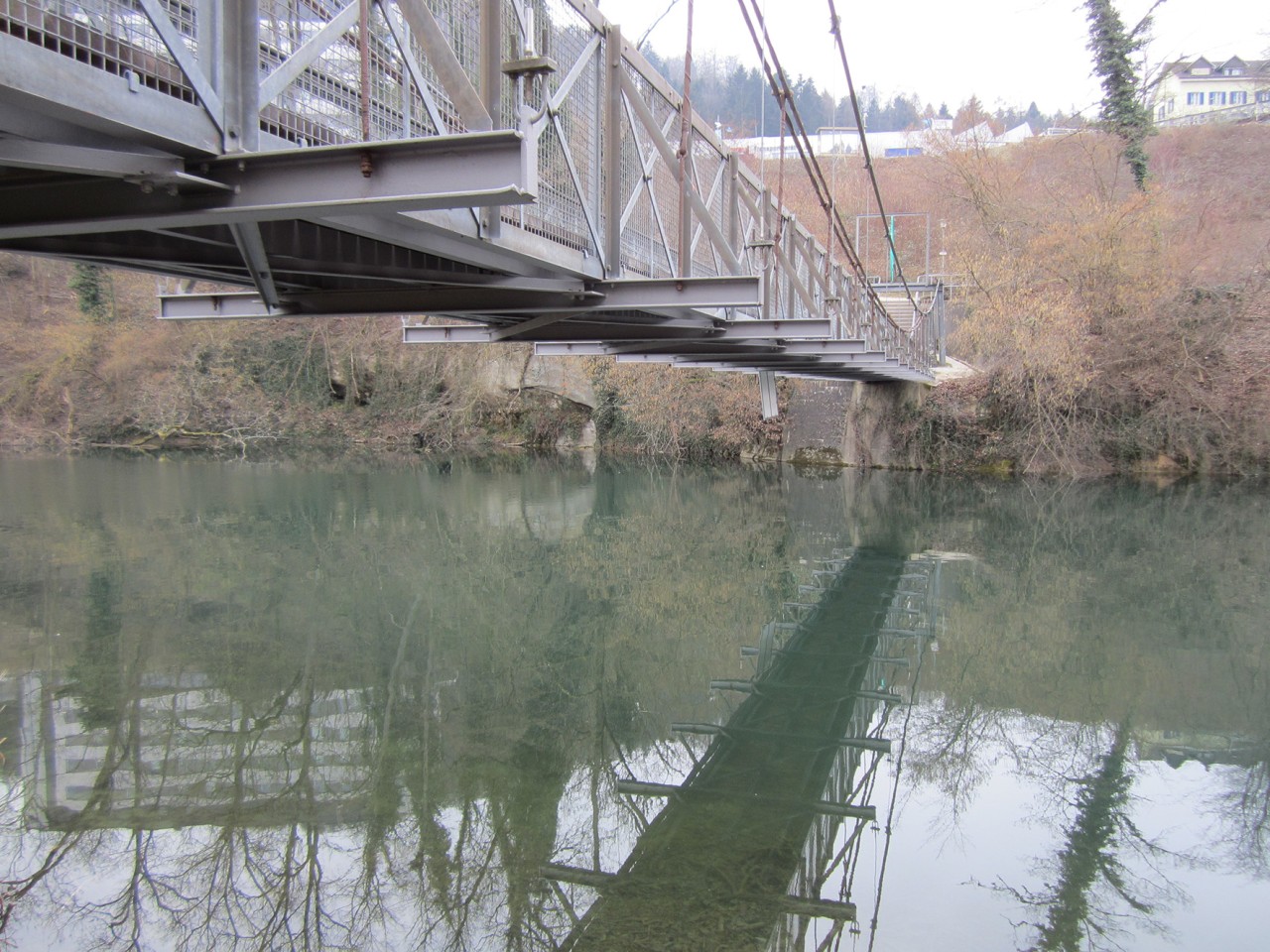 Farbfoto einer Hängebrücke über einen Fluss. Blick von unten.