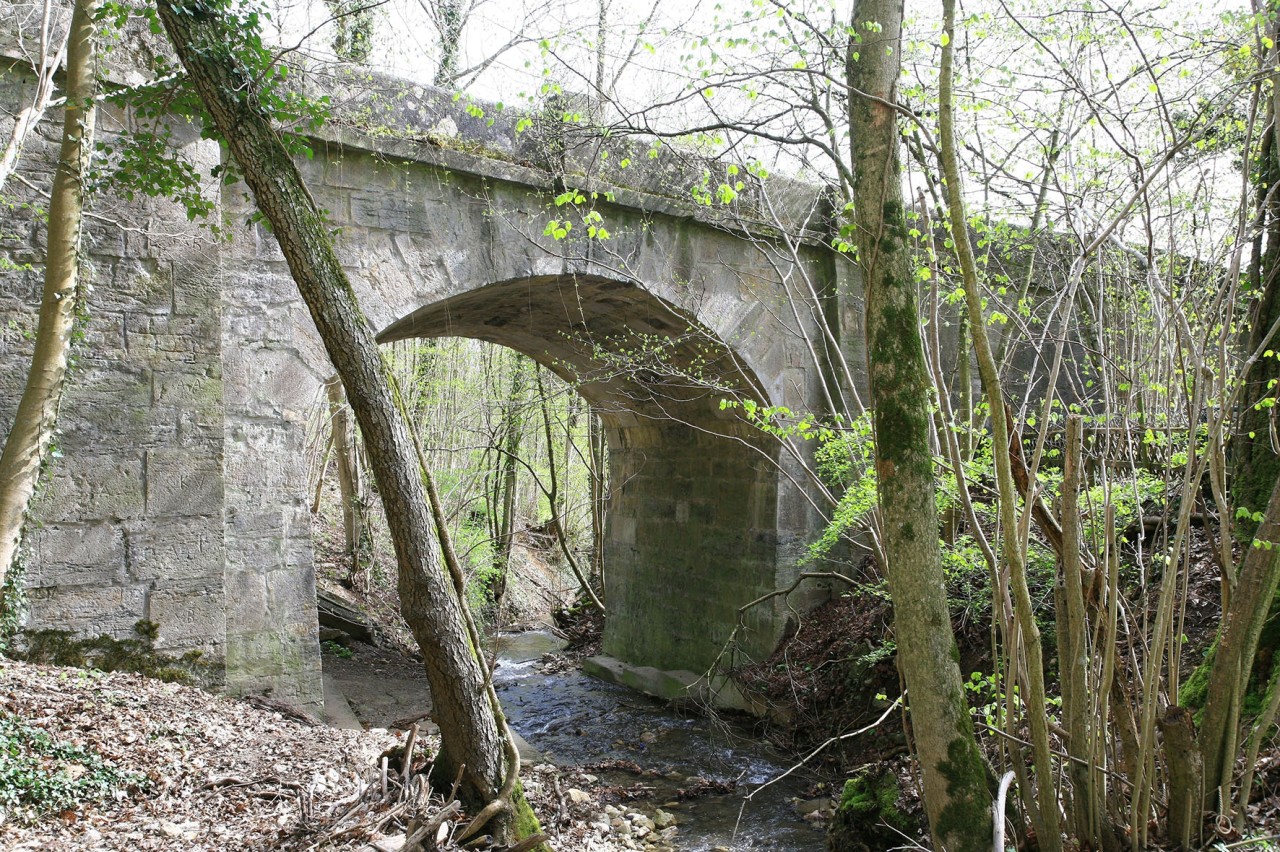 Brücke aus Stein über einen Bachlauf im Wald.