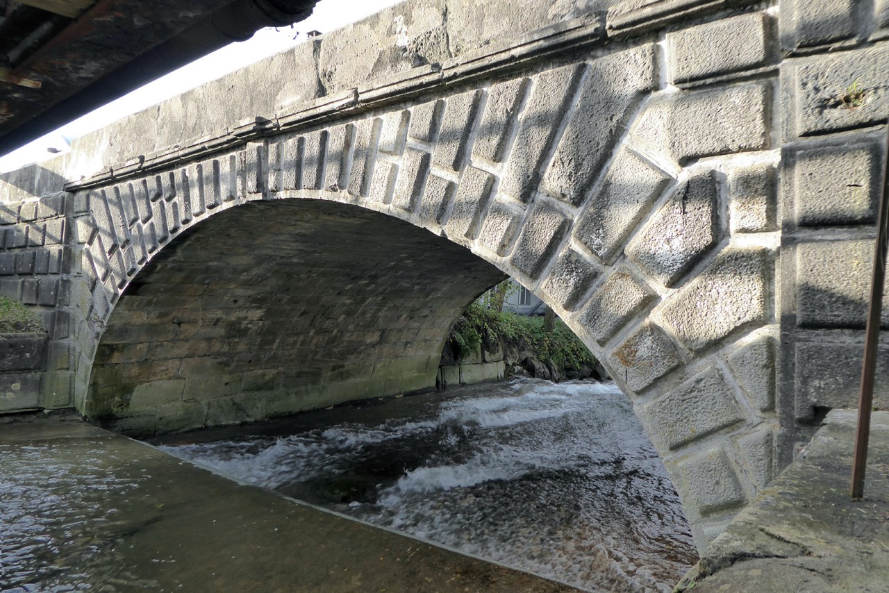 Blick von unten durch den Bogen einer Brücke aus Stein über einem Fluss.