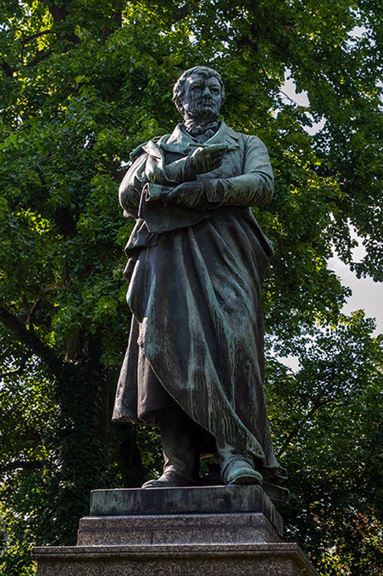 Statue eines Mannes. Im Hintergrund Bäume.
