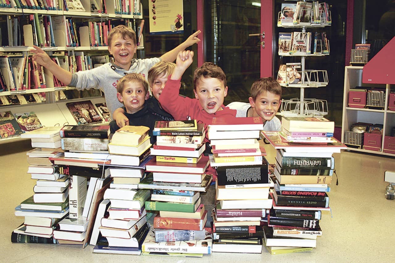 Kinder schauen lachend hinter einem Bücherhügel hervor