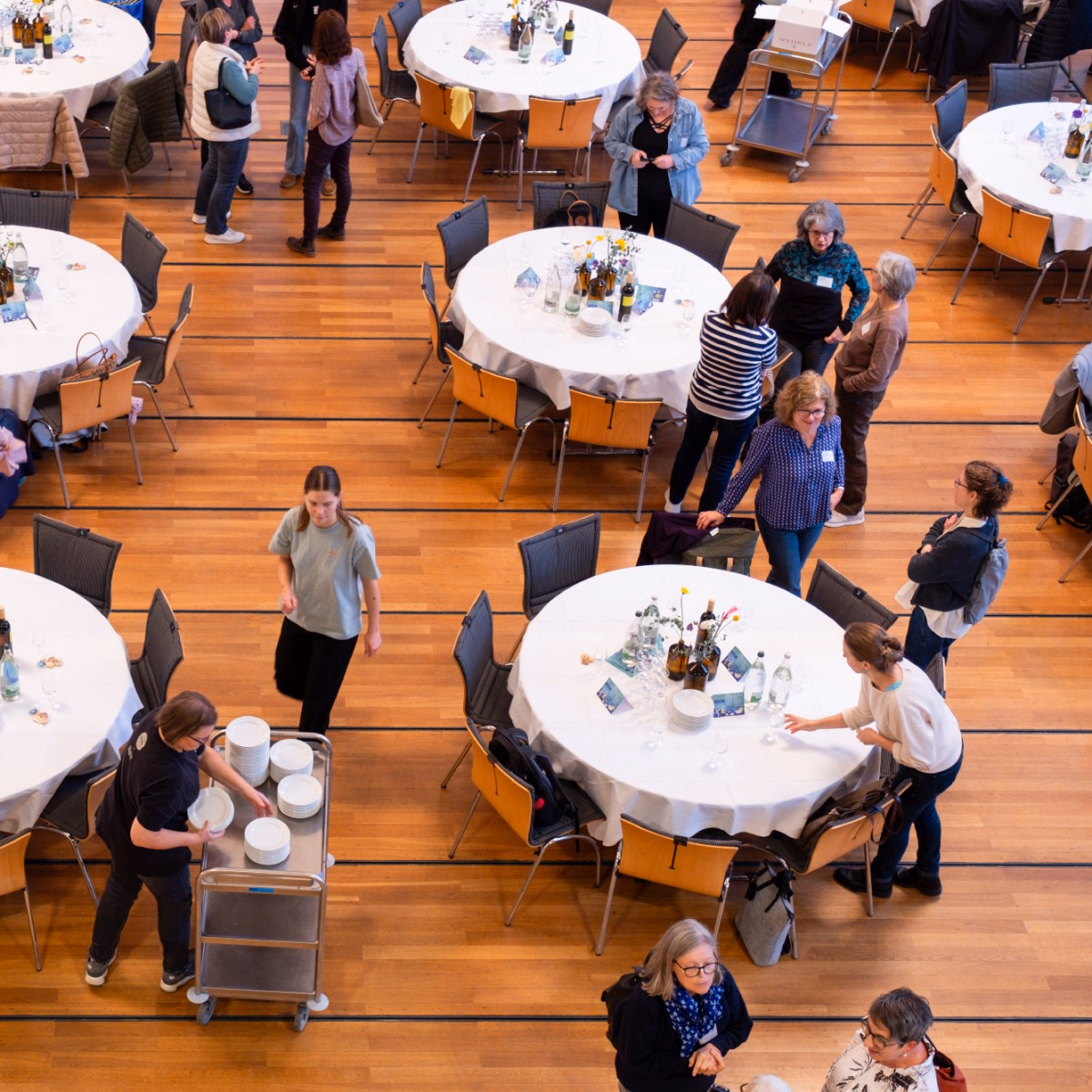 Foto von oben mit Blick auf Personen in einem Saal mit runden gedeckten Tischen.