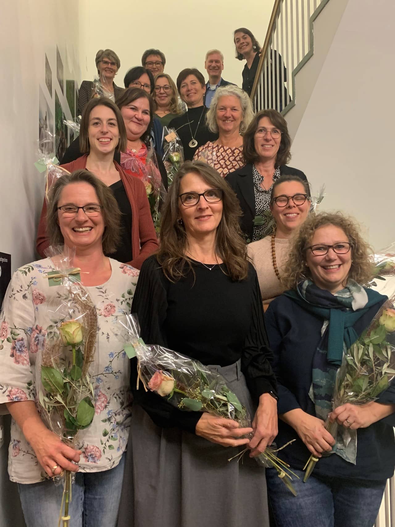 Ein Gruppe bestehend aus dreizehn Frauen steht aufgereiht auf einer Treppe. Sie halten Blumensträusse in der Hand und lächeln in die Kamera.