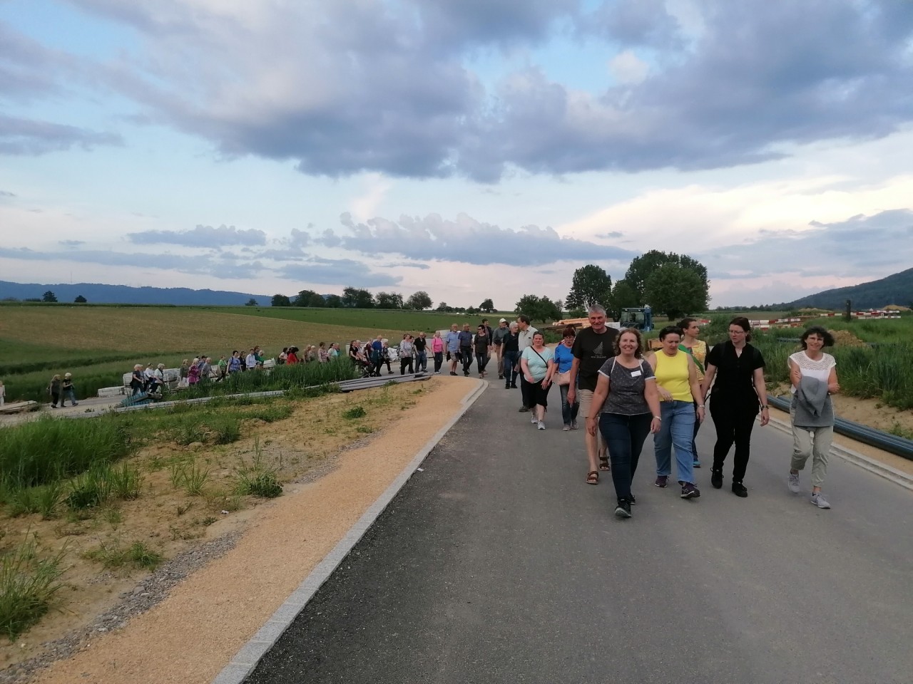 Lange Kolonne von Personen in sommerlicher Kleidung auf einer geteerten Strasse in der Natur.