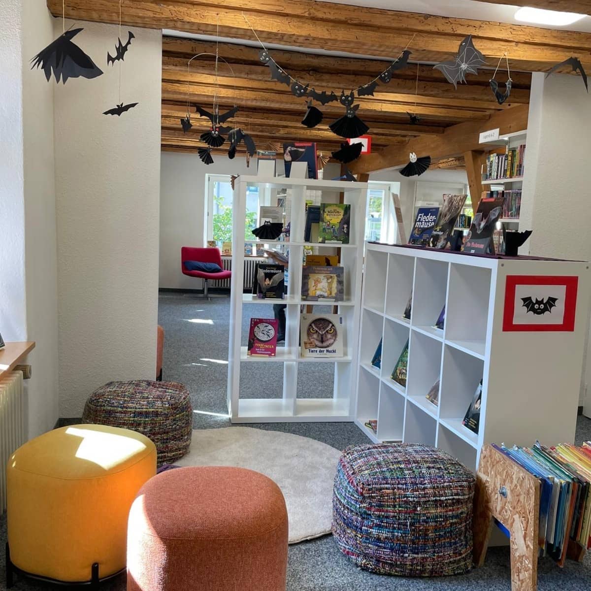 Bibliotheksraum, der mit Fledermaus-Basteleien geschmückt ist. Von der Decke hängen Fledermäuse aus Papier.  