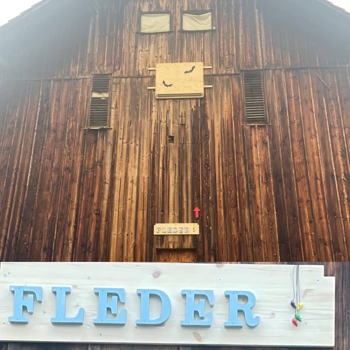 An einer Holzscheune ist gross der Schriftzug "Fleder" in hellblauen Buchstaben angebracht.
