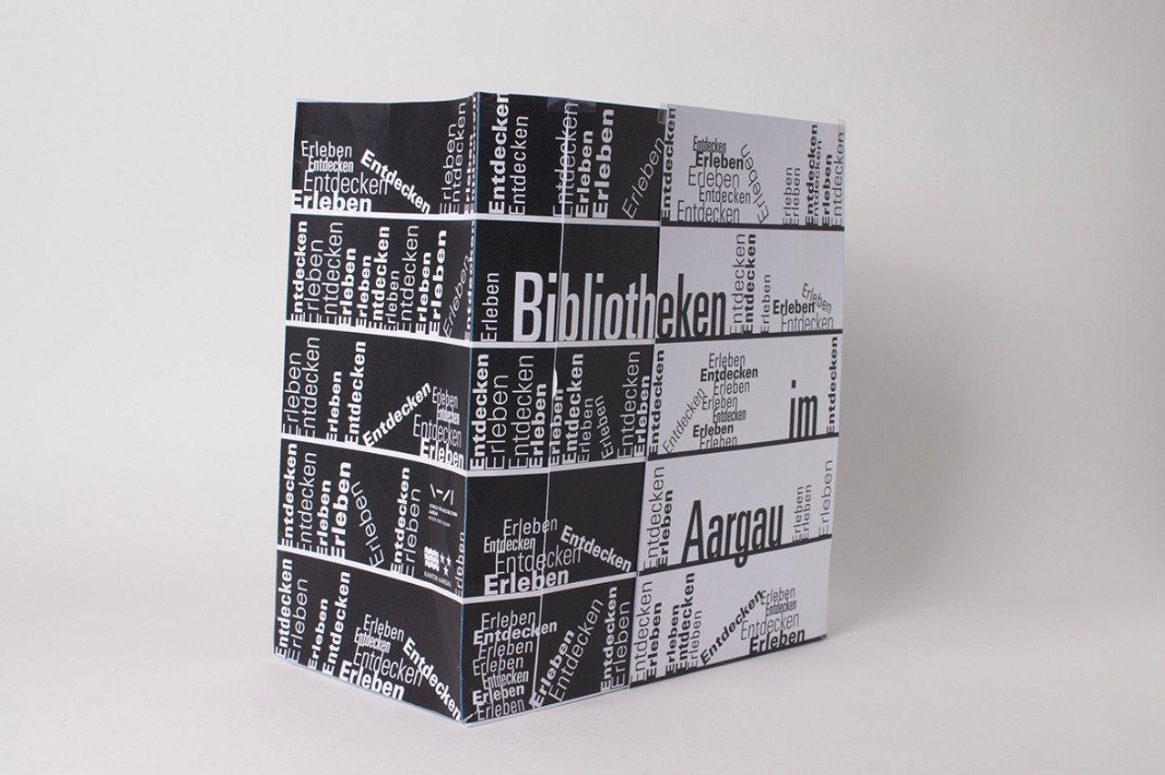 Die Maquette der Tasche aus Papier zeigt den Entwurf "Die Klassische". Die Tasche ist schlicht in schwarz-weiss gehalten und hauptsächlich typografisch gestaltet. Viele Wörter reihen sich wie Bücher auf einem Regal auf.
