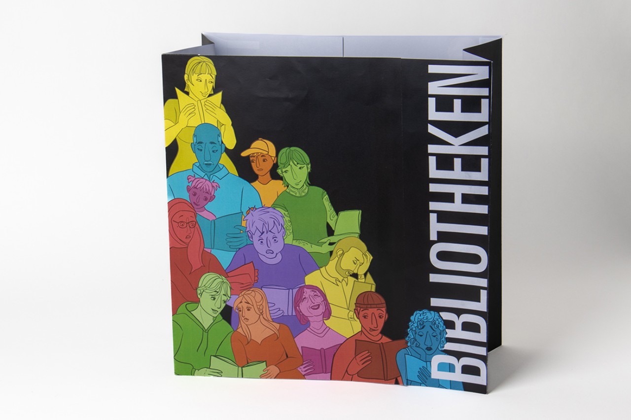 Die Maquette der Tasche aus Papier zeigt den Entwurf "Die Knallige". Darauf zu sehen sind in der unteren, linken Ecke bunt illustrierte Menschen, die lesen, singen, reden. 
